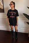 Woman wearing a black t-shirt with text and graphics, paired with black cowboy boots indoors.
