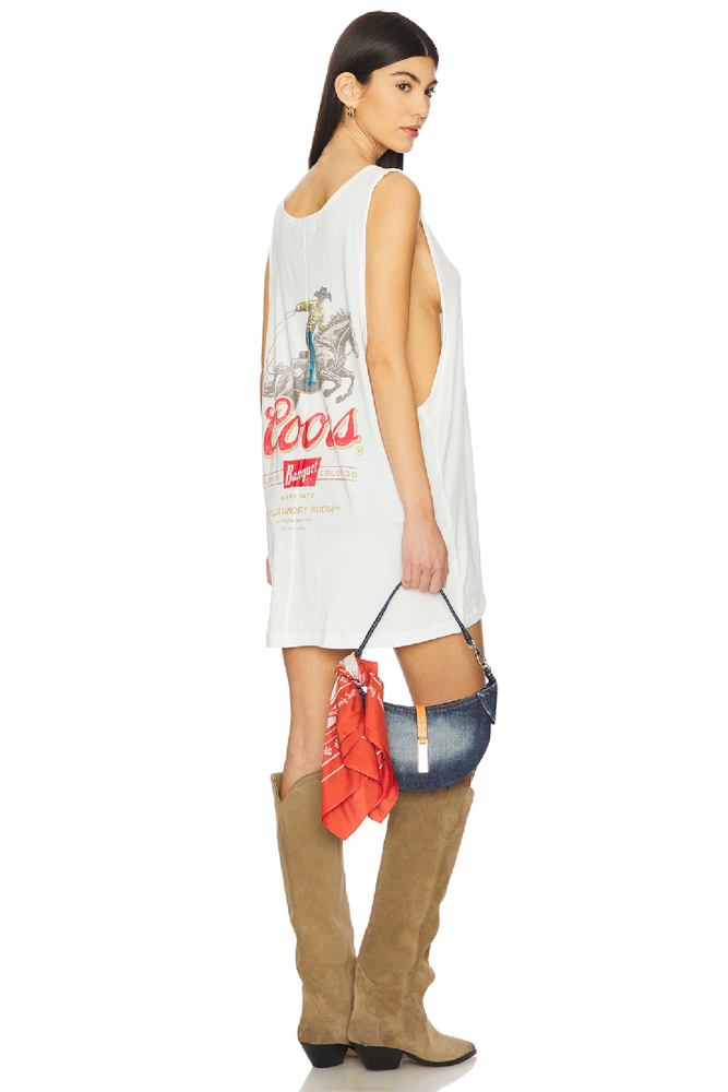 Woman wearing a white sleeveless dress with graphic Coors design and brown knee-high boots on a white background