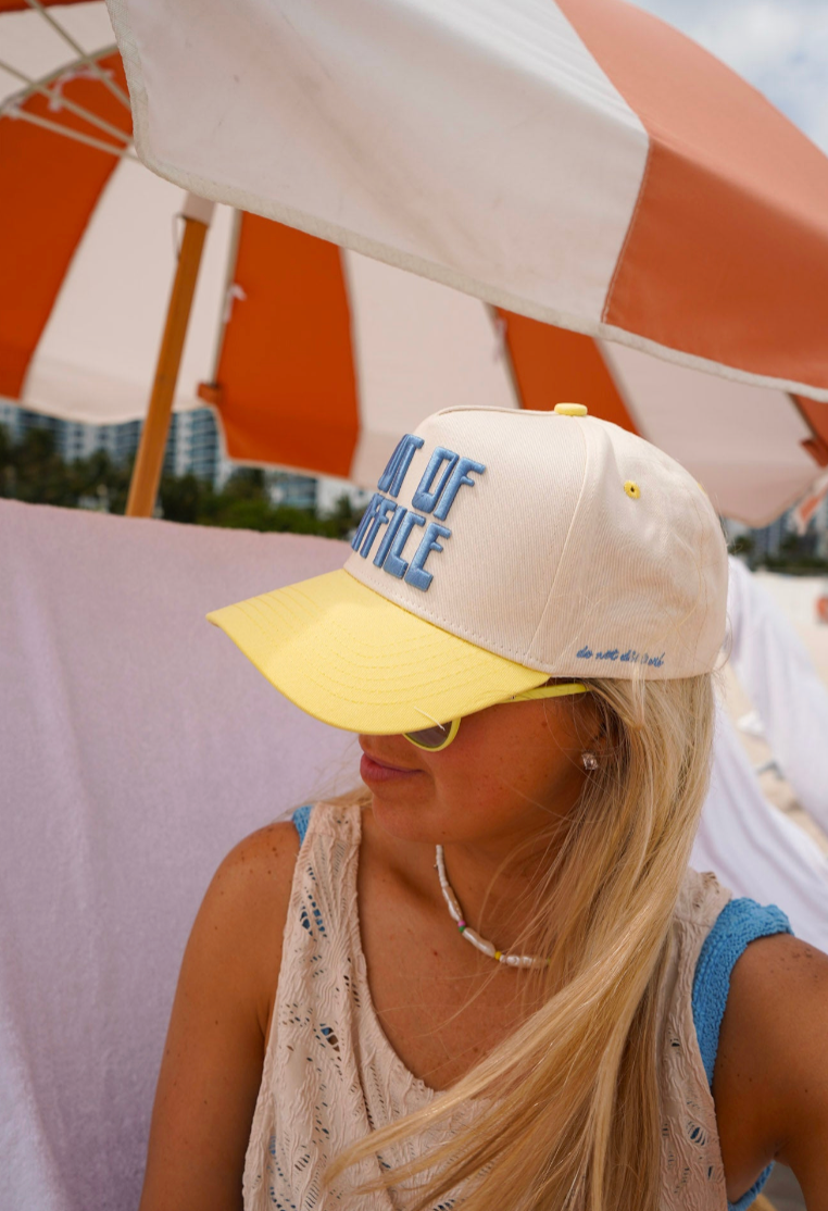 Person wearing a cap with text, sitting under a striped beach umbrella.