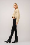 Woman wearing a beige jacket, black pants, and black boots on a plain background