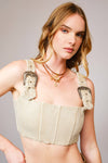 Woman wearing a beige corset with decorative straps against a plain background